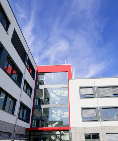 Modern white building with glass windows and a bold red accent, set against a clear blue sky.